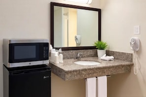 A hotel bathroom with a sink, mirror, microwave, and telephone.