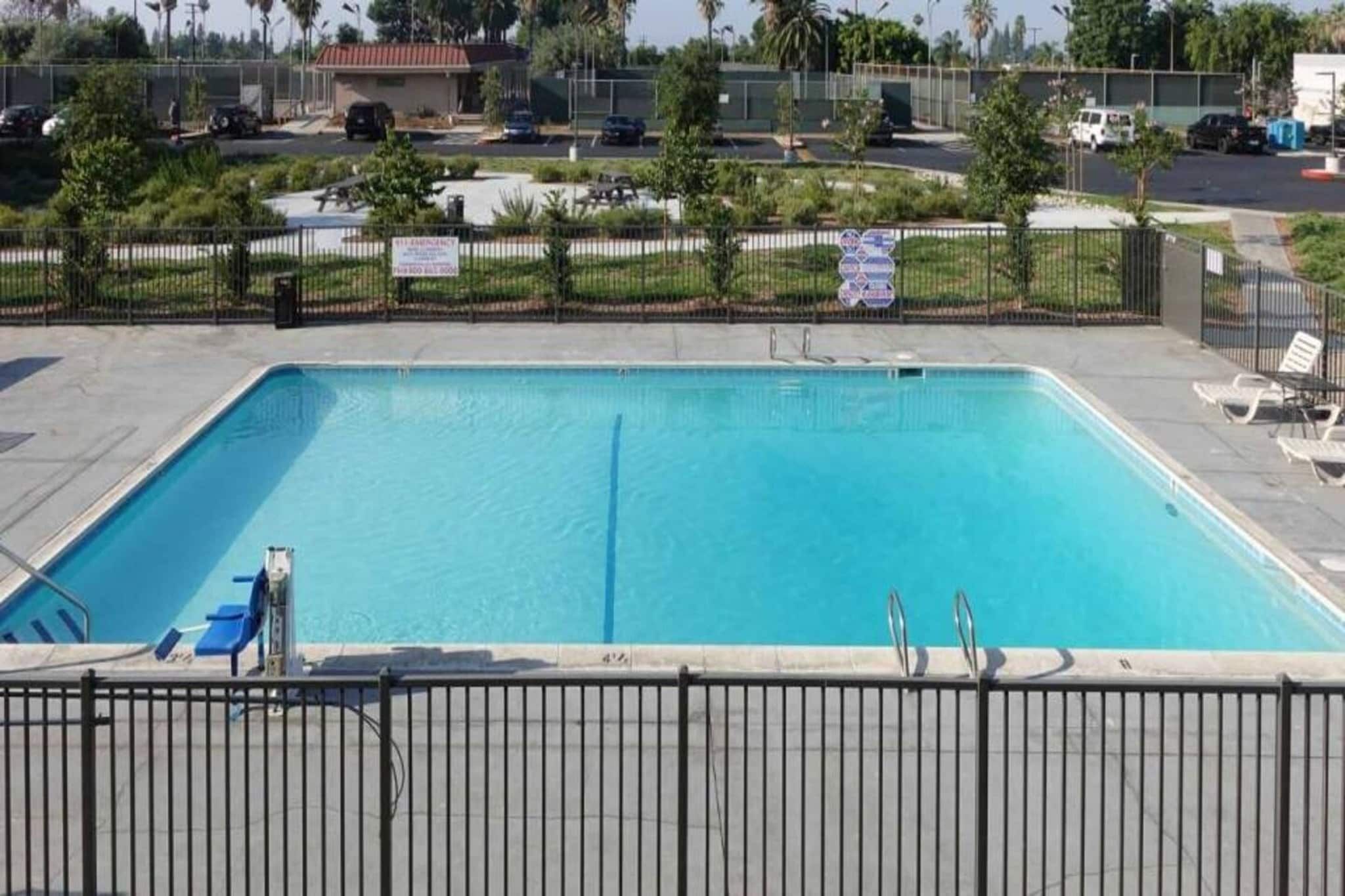 Ein rechteckiger Swimmingpool, umgeben von einem Metallzaun, mit einigen Liegestühlen und blauem Himmel im Hintergrund.