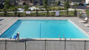 Ein rechteckiger Swimmingpool, umgeben von einem Metallzaun, mit einigen Liegestühlen und blauem Himmel im Hintergrund.