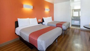 Une chambre d’hôtel avec deux lits, un plancher en bois et, au fond, une petite cuisine.