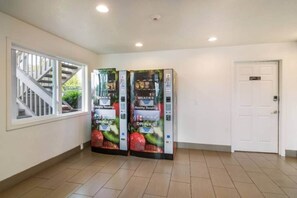 Un pasillo con dos máquinas expendedoras identificadas como 'Healthy Vending' y 'Snacks', una puerta blanca y un ventanal con vista a una escalera.