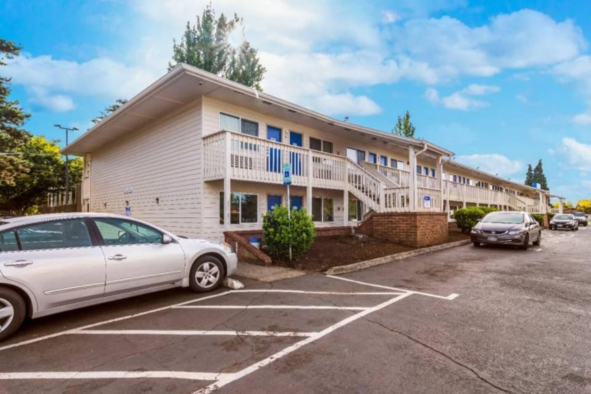 Un hôtel à plusieurs étages, doté d’un parking, d’un escalier menant à l’entrée et offrant une vue sur un ciel dégagé.
