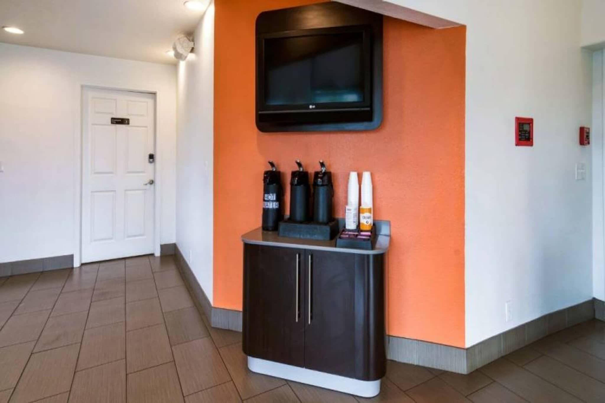 Un couloir avec un meuble noir, un téléviseur fixé sur un mur orange et une porte blanche.