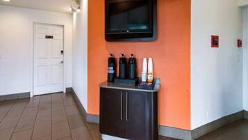 Un couloir avec un meuble noir, un téléviseur fixé sur un mur orange et une porte blanche.