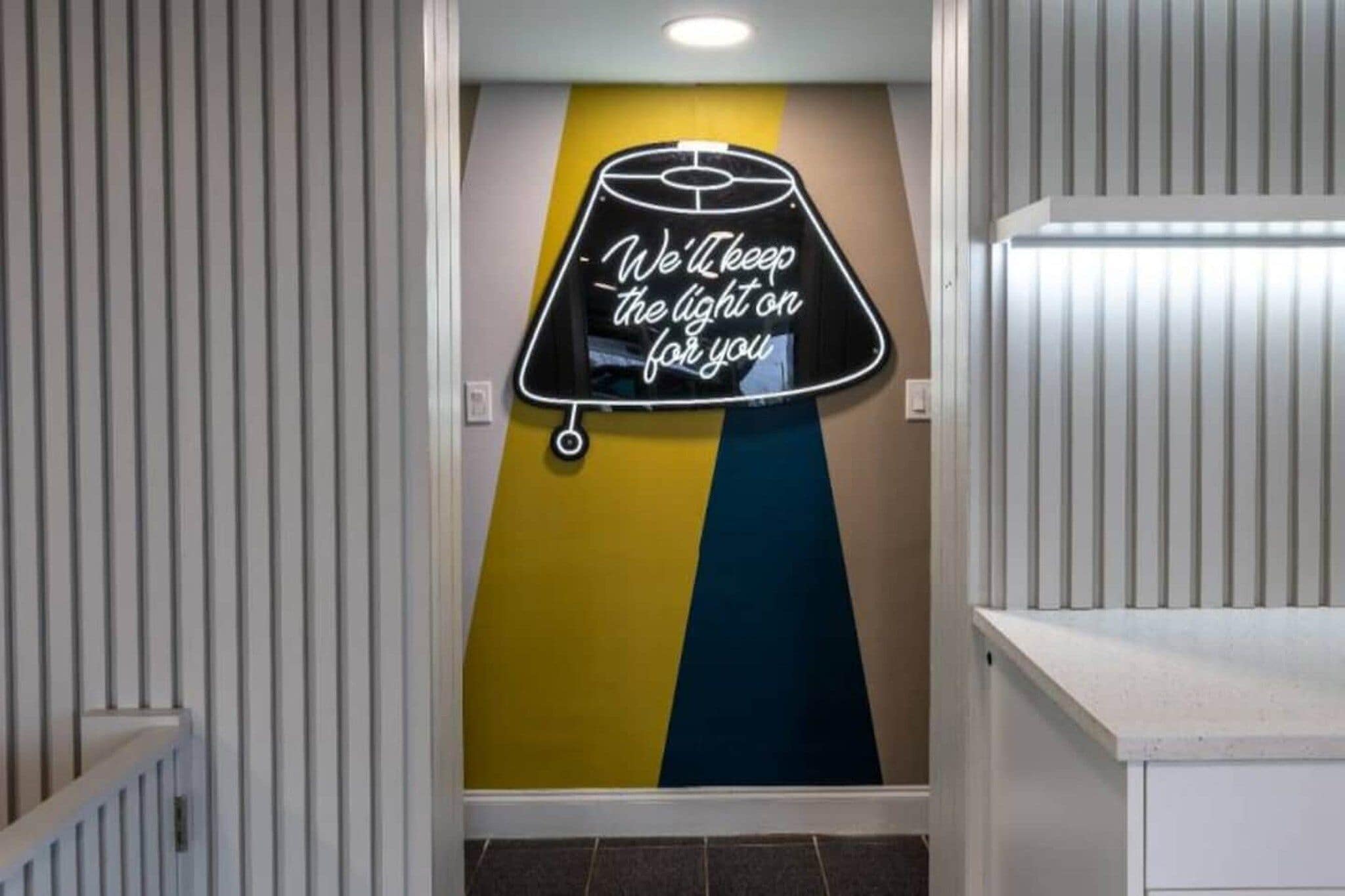 Ein Flur mit einem Neonzeichen an der Wand, auf dem steht: 'Wir lassen das Licht für Sie brennen'.