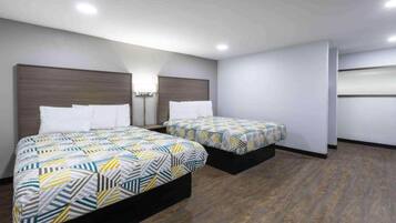 A hotel room with two beds, each with patterned bedding, a wooden headboard, a bedside table, and a wall-mounted lamp.