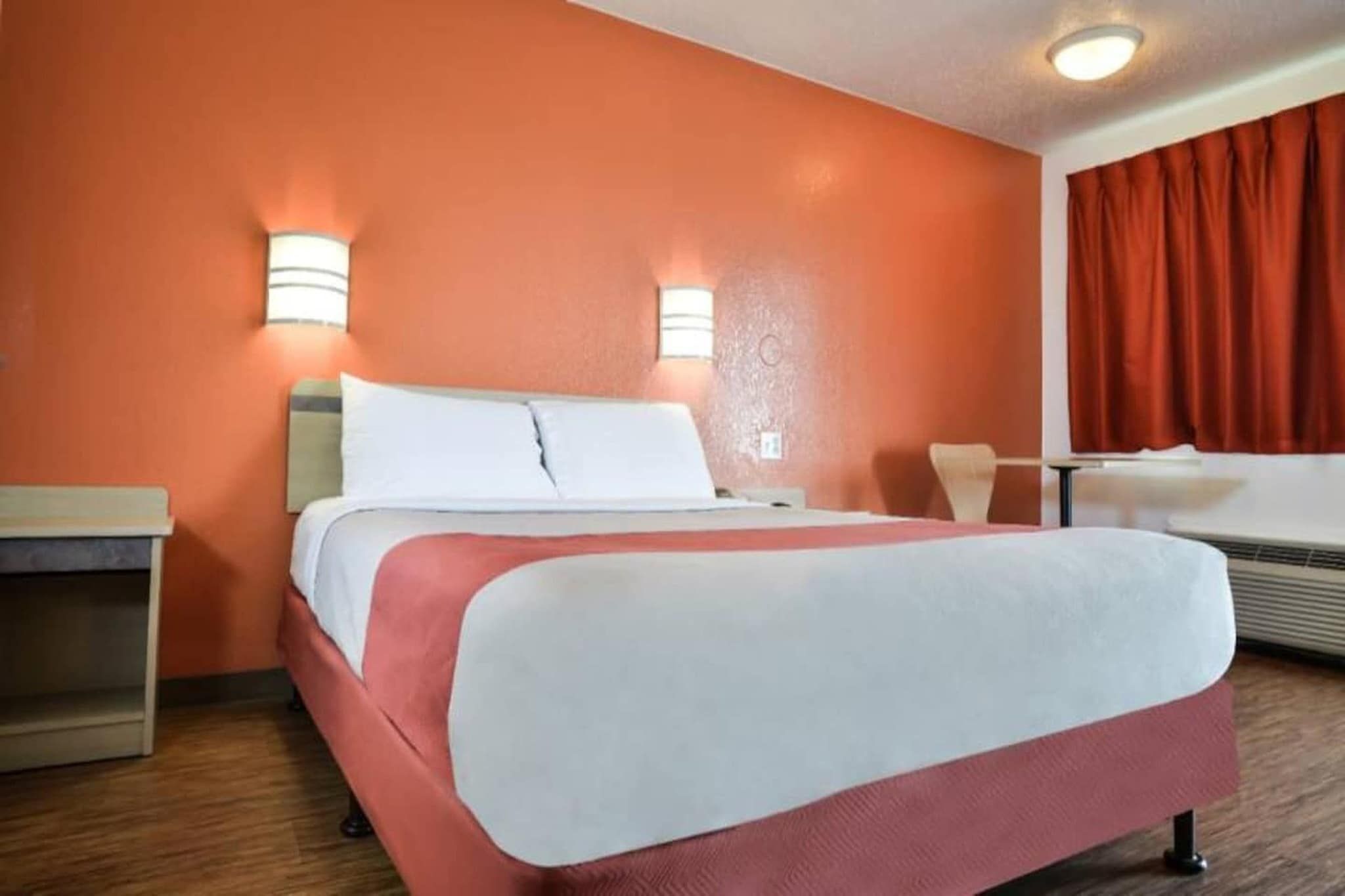 Quarto de hotel com cama, mesa de cabeceira e janela com cortinas.