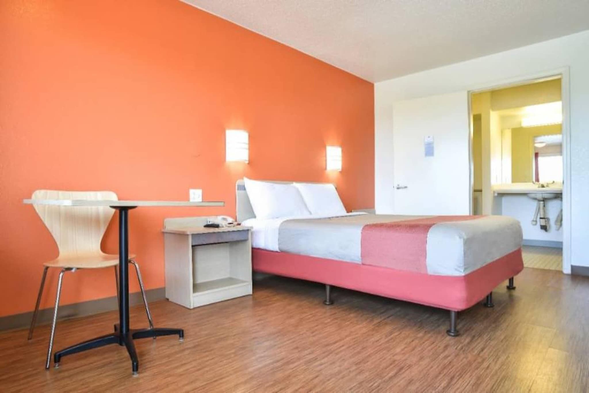 A hotel room with a bed, a desk, a chair, and a bathroom visible through an open door.