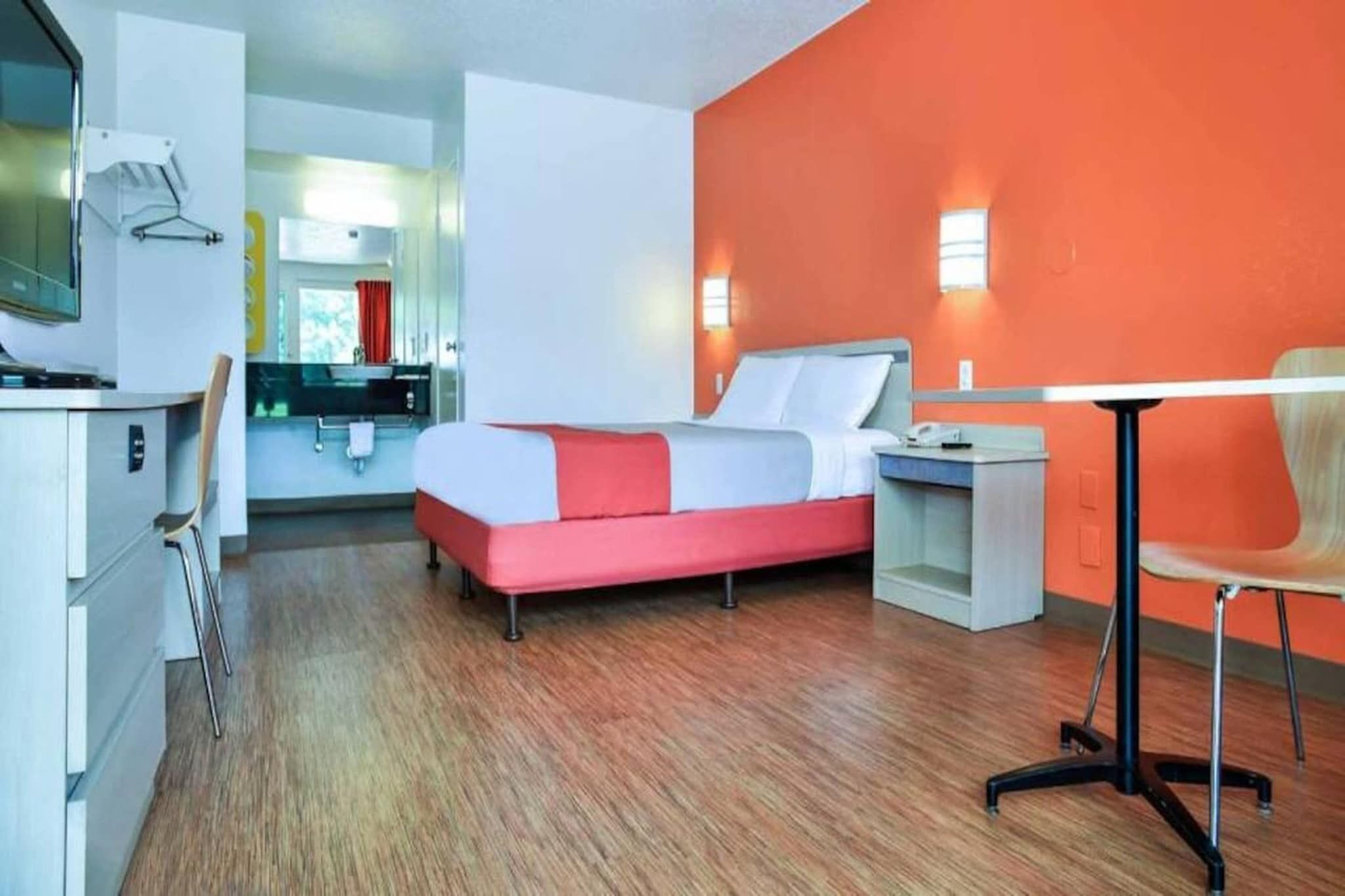 Una habitación de hotel con una cama, mesita de noche, silla y un escritorio con otra silla.