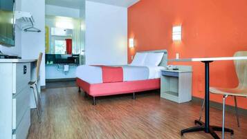 Una habitación de hotel con una cama, mesita de noche, silla y un escritorio con otra silla.