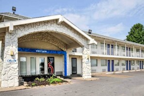 Un motel con ingresso ad arco in pietra, un cartello di benvenuto e un parcheggio.