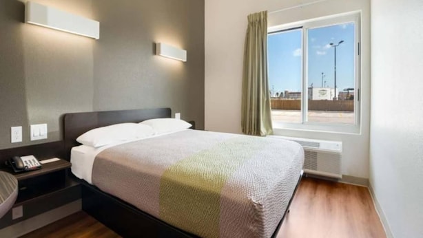 A hotel room with a bed, bedside table, phone, and a window with curtains. - 1 Queen Bed | Non-Smoking (Corpus Christi TX)