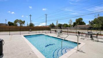 A rectangular swimming pool with a metal ladder, surrounded by a concrete deck and a metal fence.