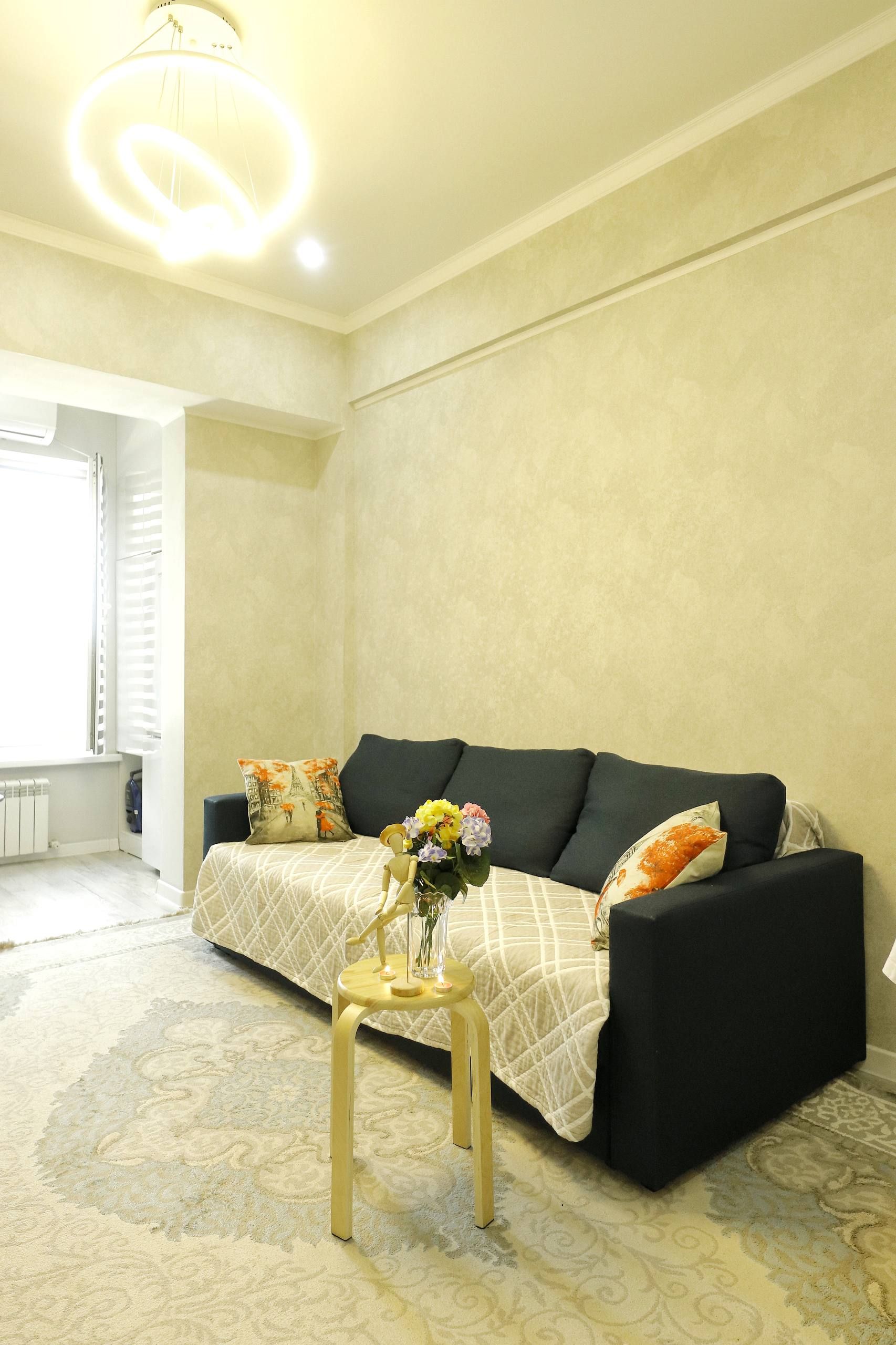A living room with a black sofa, a small wooden table with a vase of flowers, and a patterned rug.
