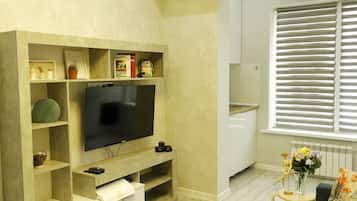 Ein modernes Wohnzimmer mit Flachbildfernseher, eingebauten Regalen, einem gemusterten Teppich und einem Fenster mit Jalousien.