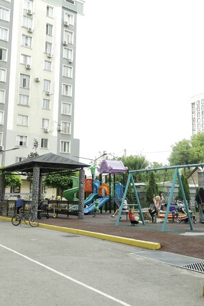 Un parque infantil con toboganes y columpios, una zona de estar cubierta y una bicicleta estacionada cerca.