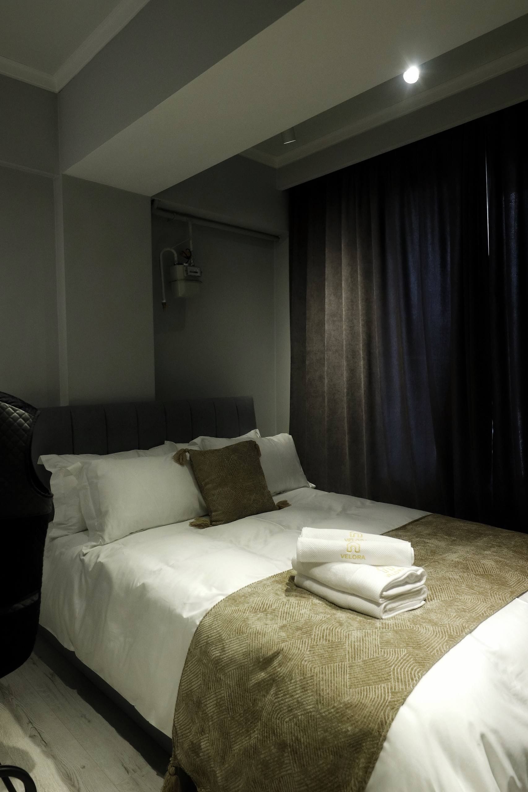 A hotel room with a bed, a headboard, a bedside table, and a curtain.