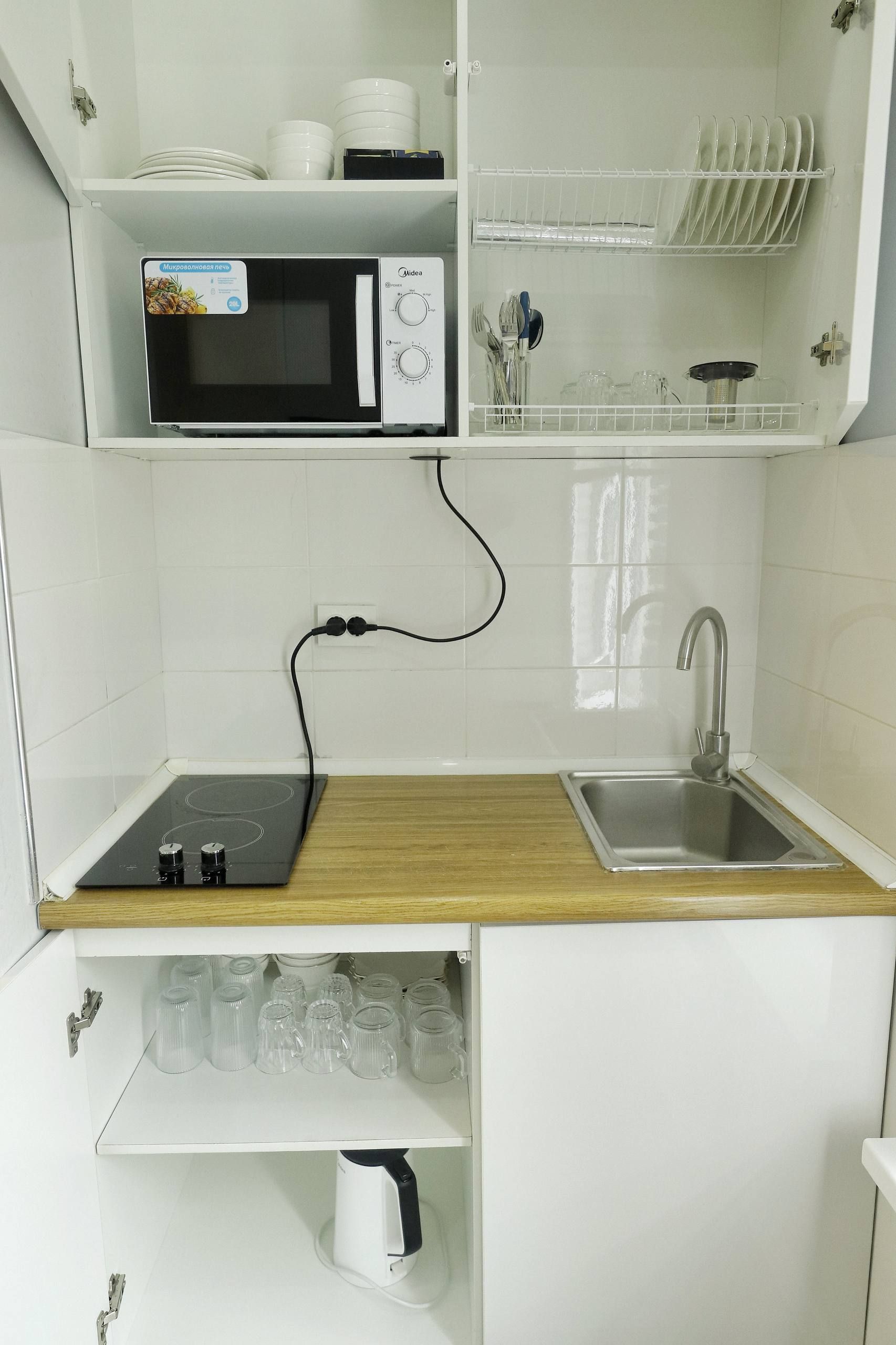 A compact kitchen with a microwave, stove, sink, and storage shelves.