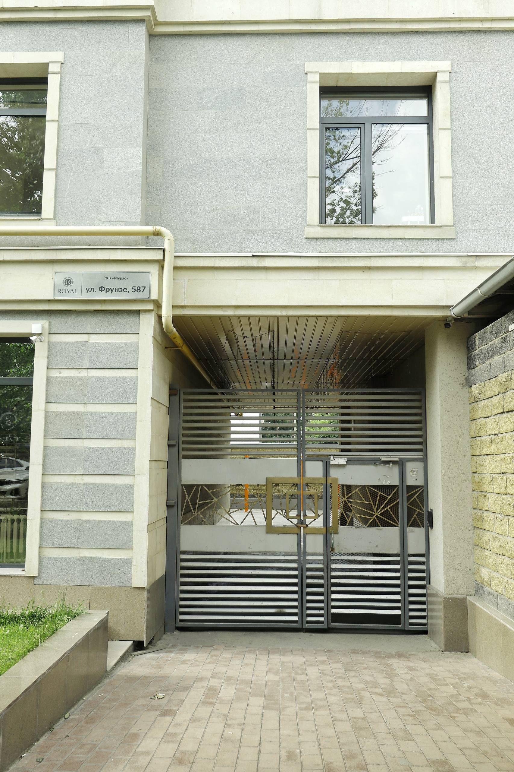 A building entrance with a metal gate, a sign with Cyrillic text, and a paved pathway leading to the entrance.