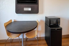 A compact room with a small round table and two chairs, a microwave on a cabinet, and a wall-mounted television. - 2 Full Beds | Micfridge (Ventura)