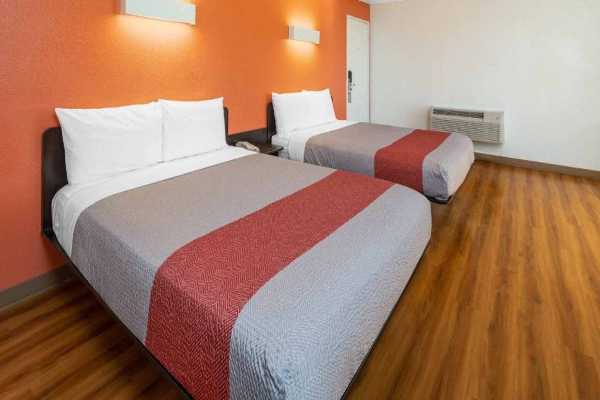 A hotel room with two beds, each with white pillows and grey bedding with a red accent.