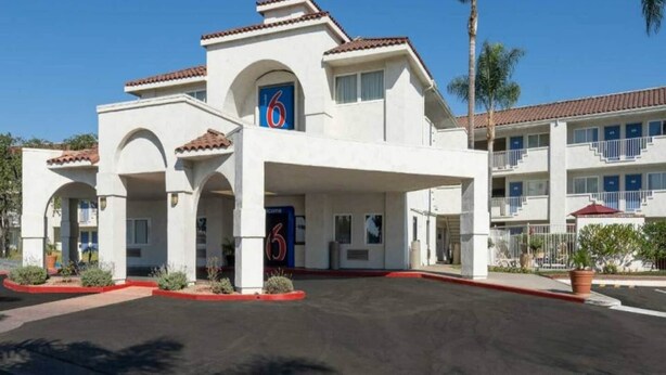 Un hotel de varios pisos con entrada central, varios balcones y un estacionamiento.