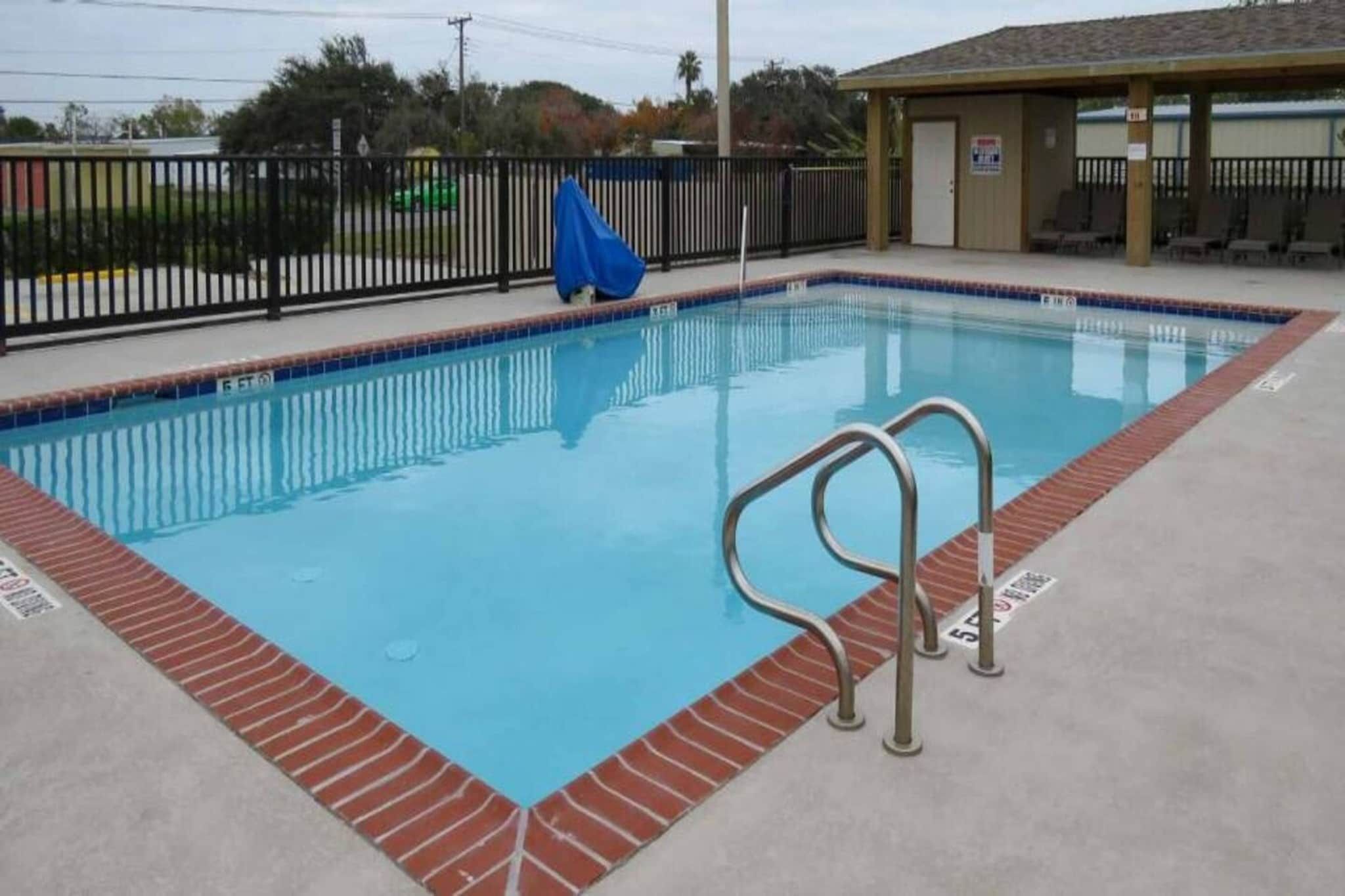 Una piscina rectangular con una escalera metálica en un lateral, rodeada por un borde de ladrillo.