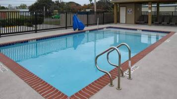 Una piscina rectangular con una escalera metálica en un lateral, rodeada por un borde de ladrillo.
