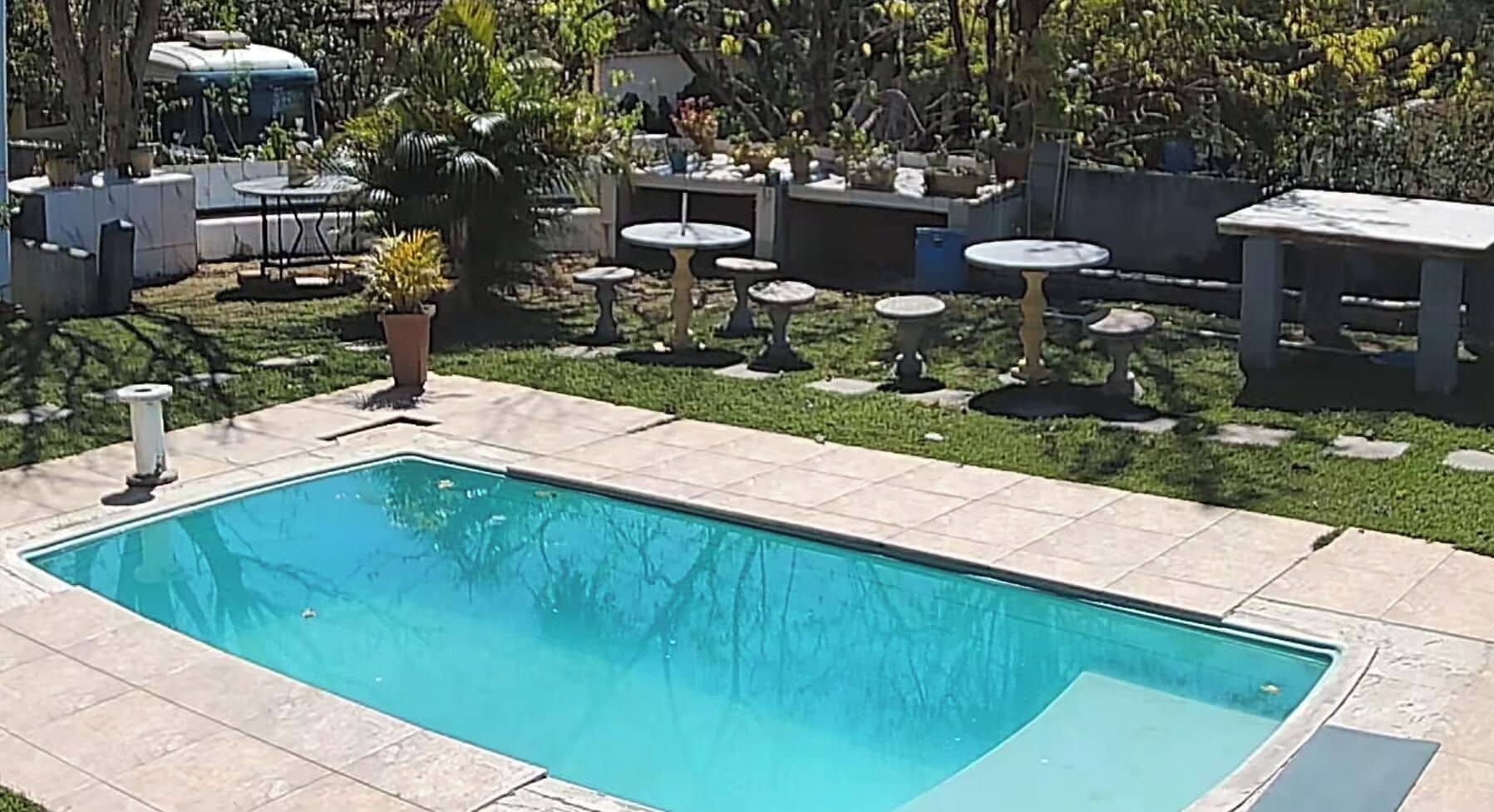 A rectangular swimming pool with a tiled deck, surrounded by outdoor furniture and potted plants.
