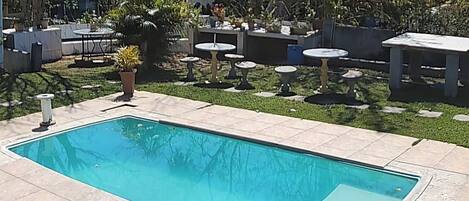 A rectangular swimming pool with a tiled deck, surrounded by outdoor furniture and potted plants.