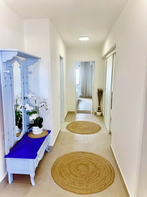 A hallway with a blue bench, white potted orchids, and two woven mats on the floor. - Delightful 2-bedroom oceanview apartment with AC in Quarteira (Quarteira)