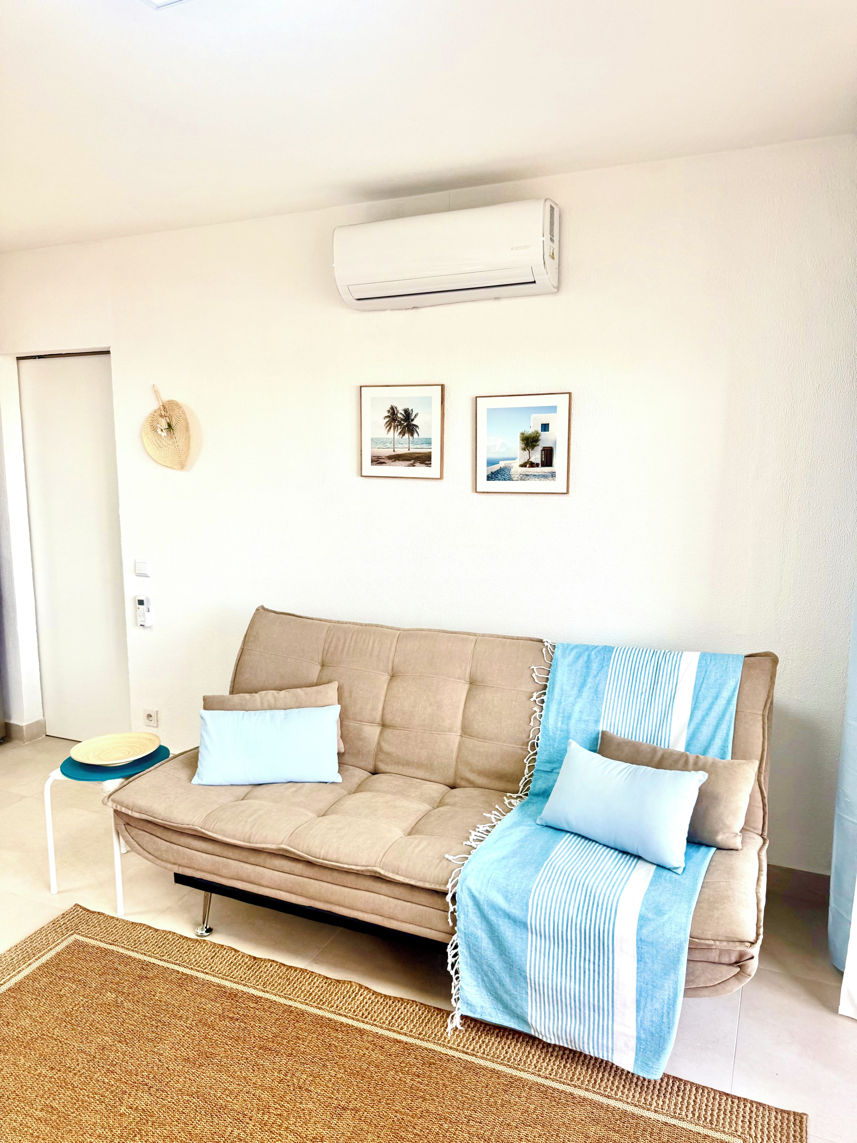Un salon avec un canapé beige, un plaid rayé bleu et blanc, un tapis tissé et deux tableaux encadrés accrochés au mur.