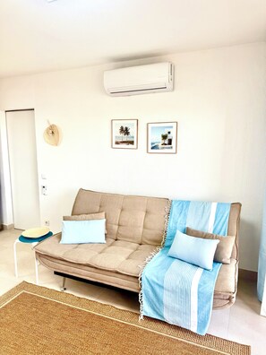 Un salon avec un canapé beige, un plaid rayé bleu et blanc, un tapis tissé et deux tableaux encadrés accrochés au mur.