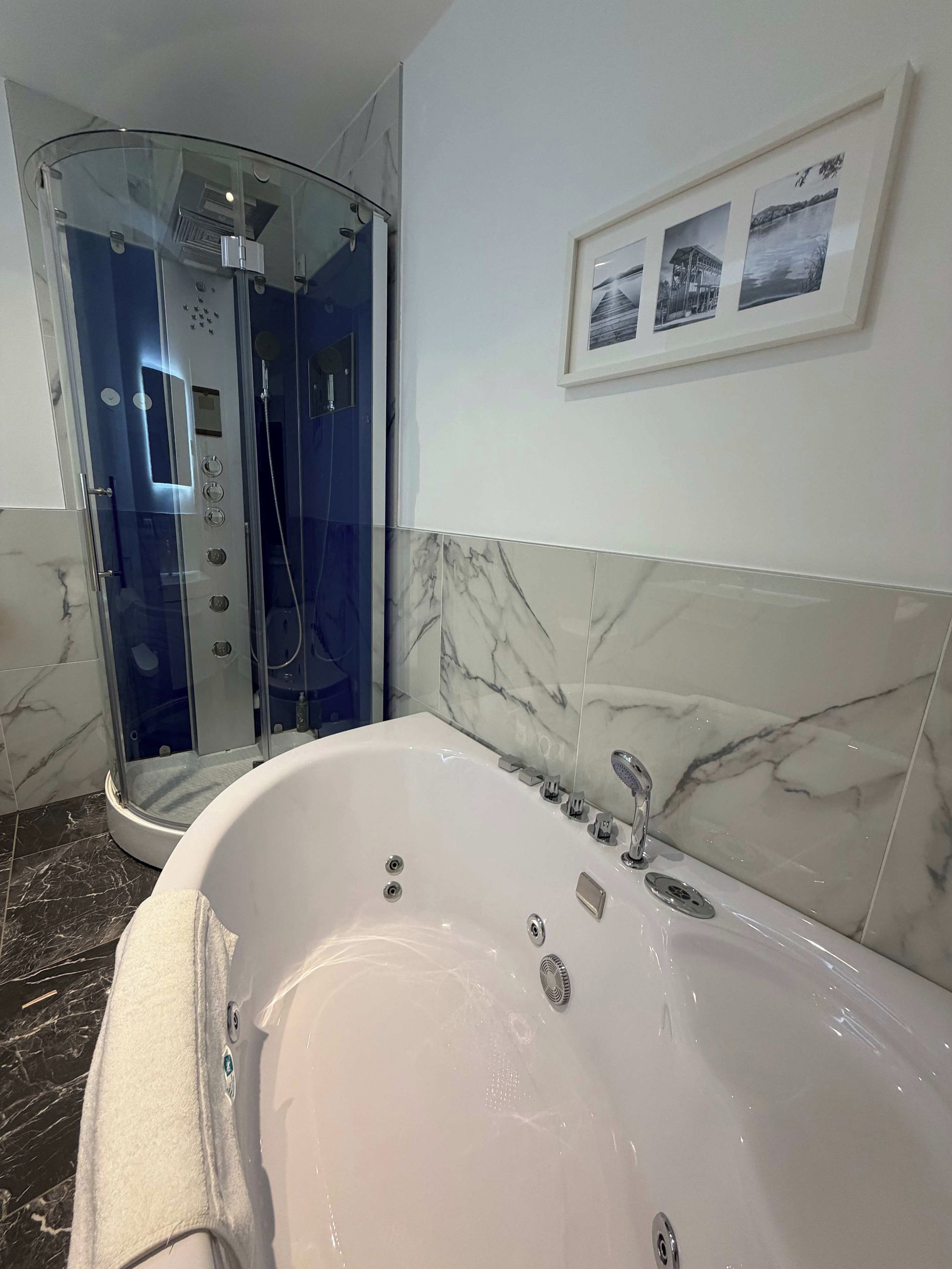 Ein modernes Badezimmer mit einer begehbaren Glasdusche, einer großen Badewanne und Marmorwänden.