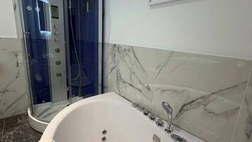 Ein modernes Badezimmer mit einer begehbaren Glasdusche, einer großen Badewanne und Marmorwänden.