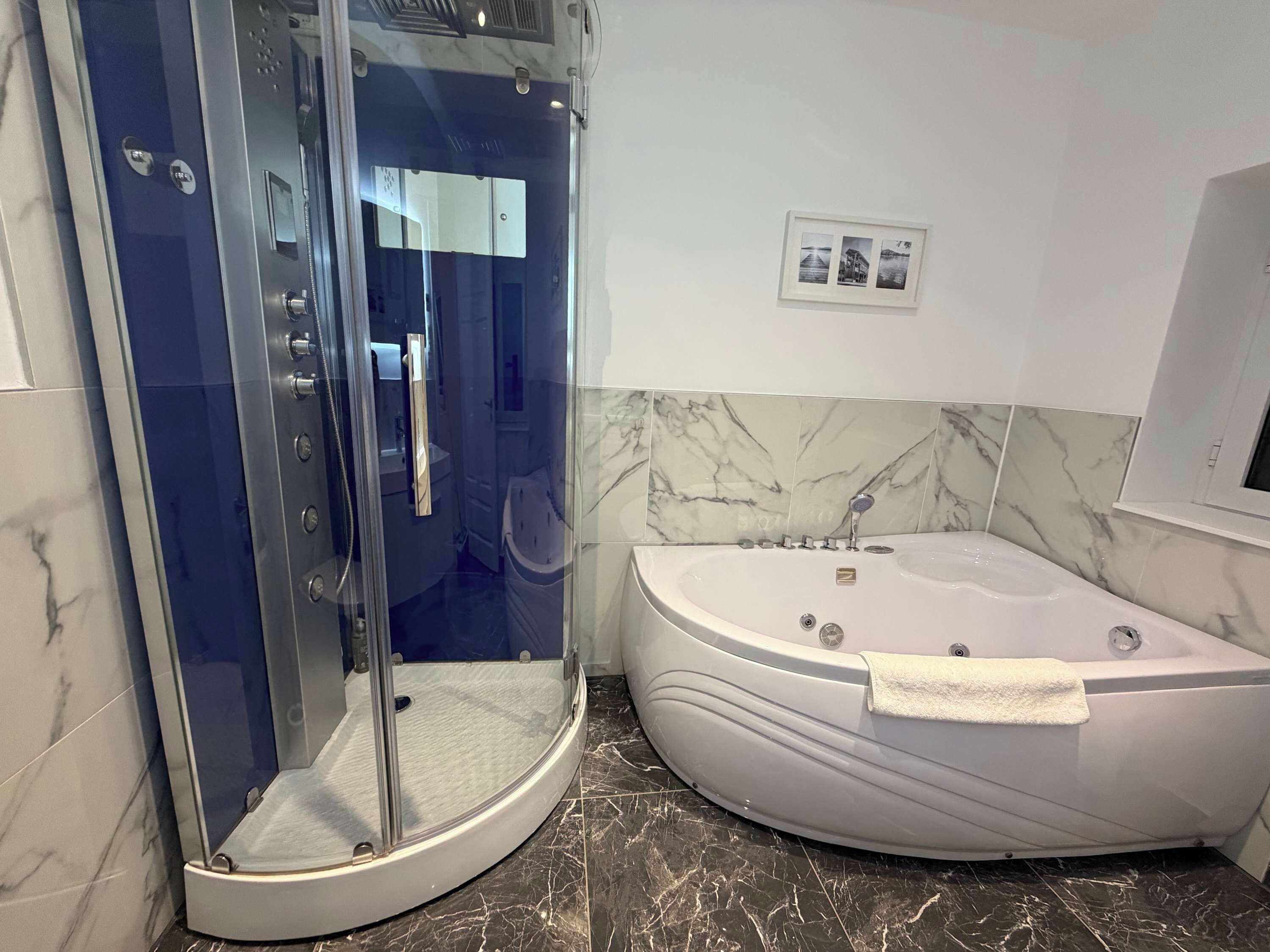 Ein modernes Badezimmer mit einer gläsernen Duschkabine, einer freistehenden Badewanne und marmorierten Wänden.