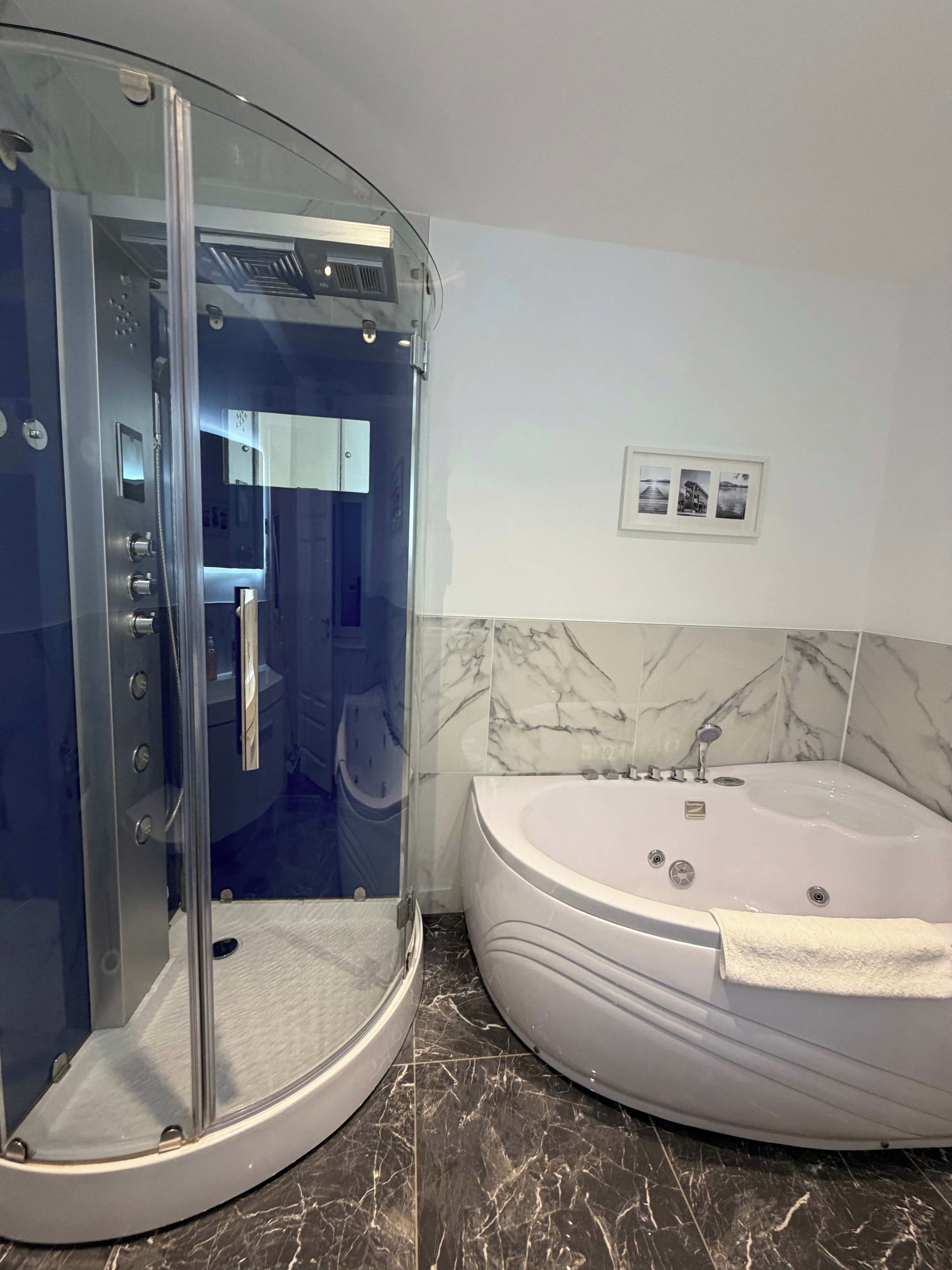 A bathroom with a glass-enclosed shower, a white bathtub, and marble flooring.
