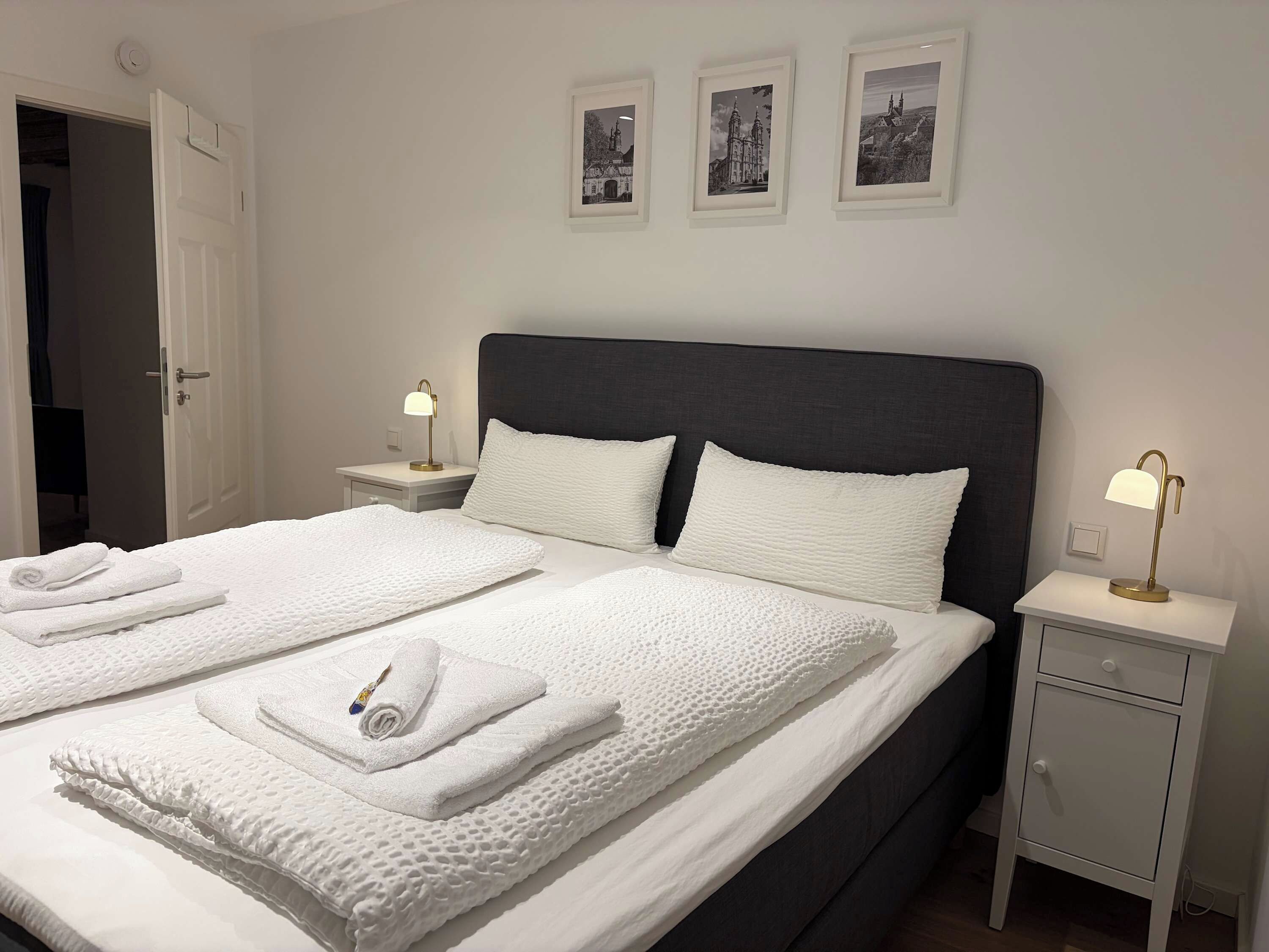 Ein Hotelzimmer mit einem Doppelbett, zwei Nachttischen, einem Beistelltisch und drei gerahmten Bildern an der Wand.