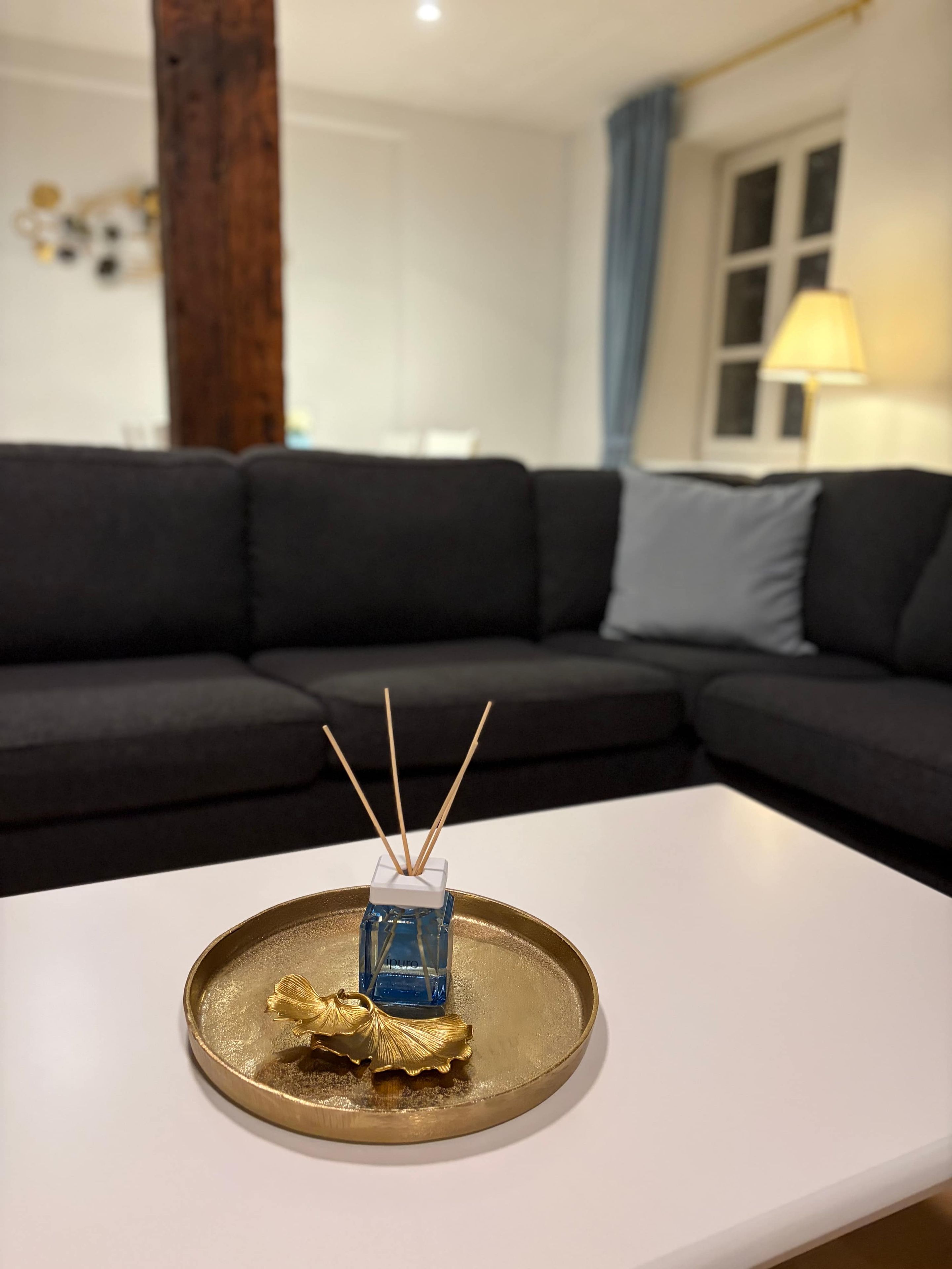 Ein modernes Wohnzimmer mit einem weißen Couchtisch, einem blauen Glasdiffusor mit Schilfrohlingen und Blattgolddekor.
