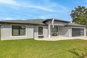 A modern two-story house with a grey exterior, a sloped roof, and a well-maintained lawn. - Outdoor Oasis! Luxe Waterfront Gem in Lehigh Acres (Lehigh Acres)