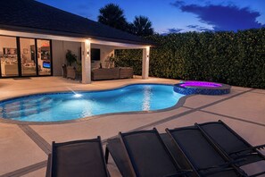 A swimming pool with a hot tub, lounge chairs, and a covered patio area. - Outdoor Oasis! Luxe Waterfront Gem in Lehigh Acres (Lehigh Acres)