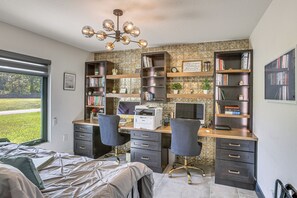 Een moderne slaapkamer met een groot bed, een bureau met twee stoelen, een computer en een boekenkast.
