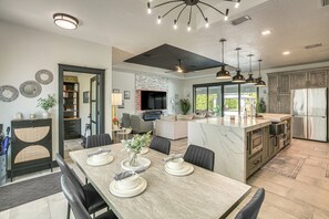 Een moderne keuken met een centraal eiland, een eethoek met stoelen en een grote flatscreen televisie aan de muur.