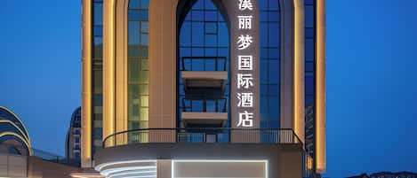 A hotel with a modern architectural design, featuring a prominent arched entrance and illuminated signage.