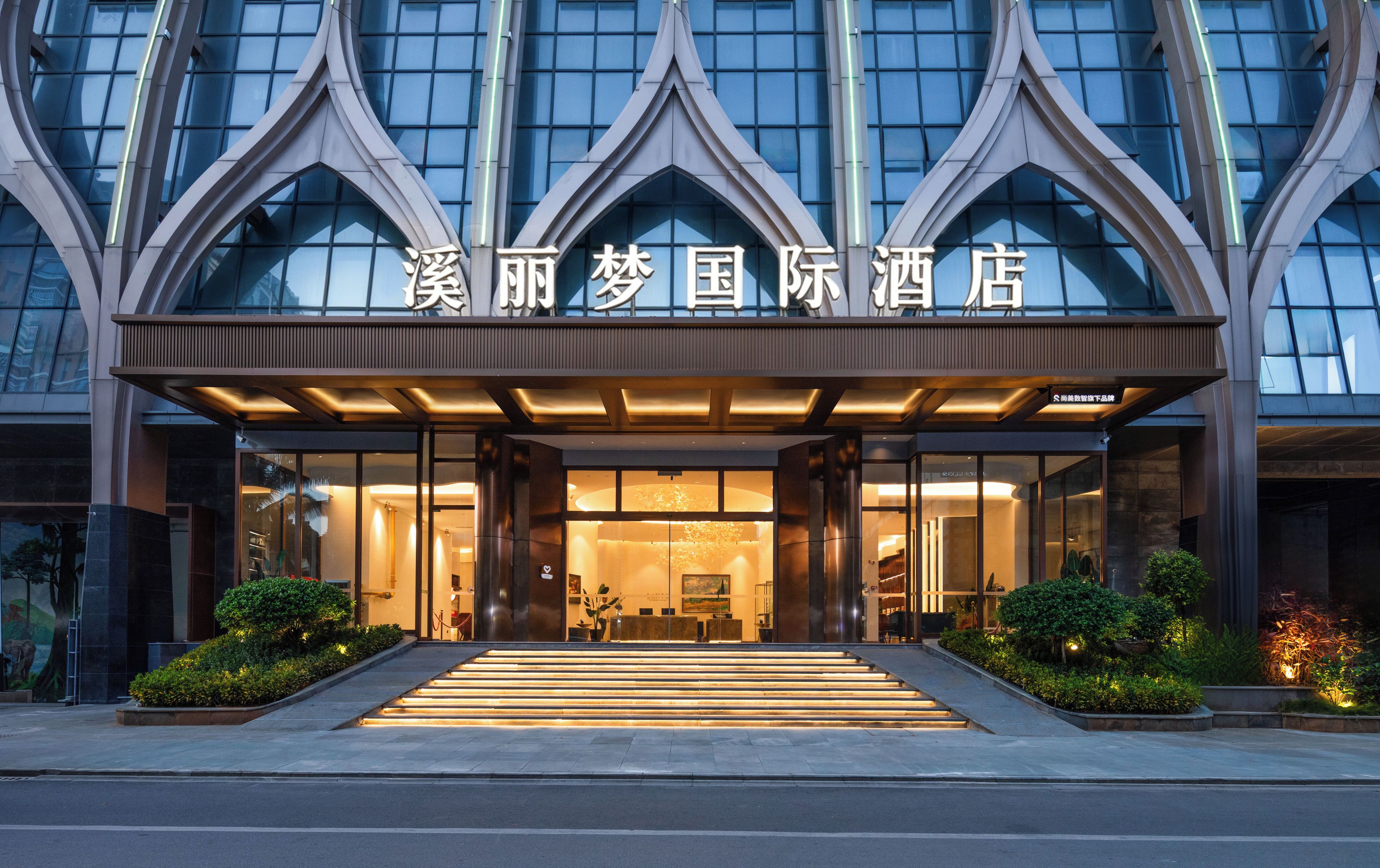 A hotel entrance with a modern design, featuring a glass facade and a prominent entrance with steps leading up to it.