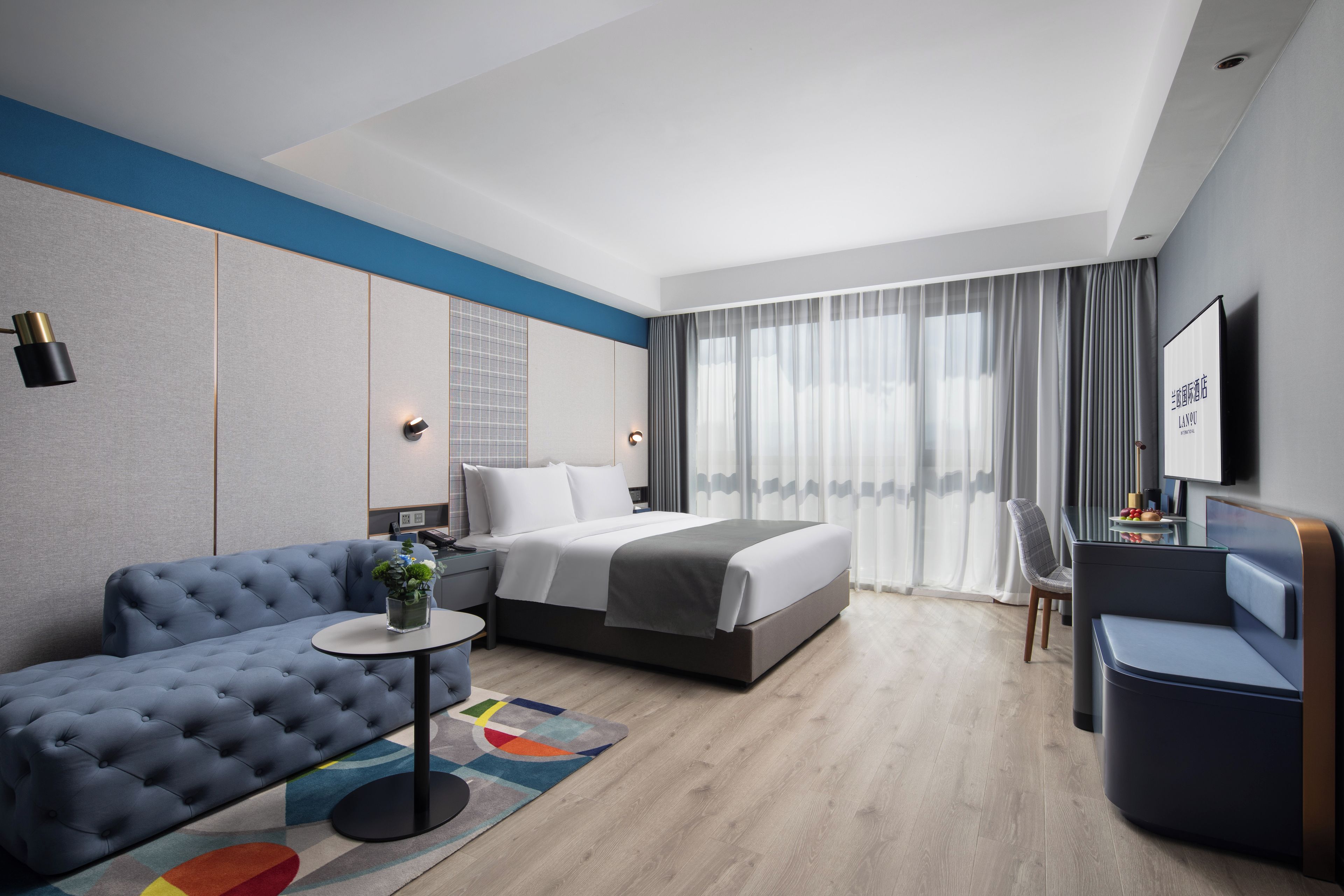 A modern hotel room with a bed, a sofa, a small table, and a chair.