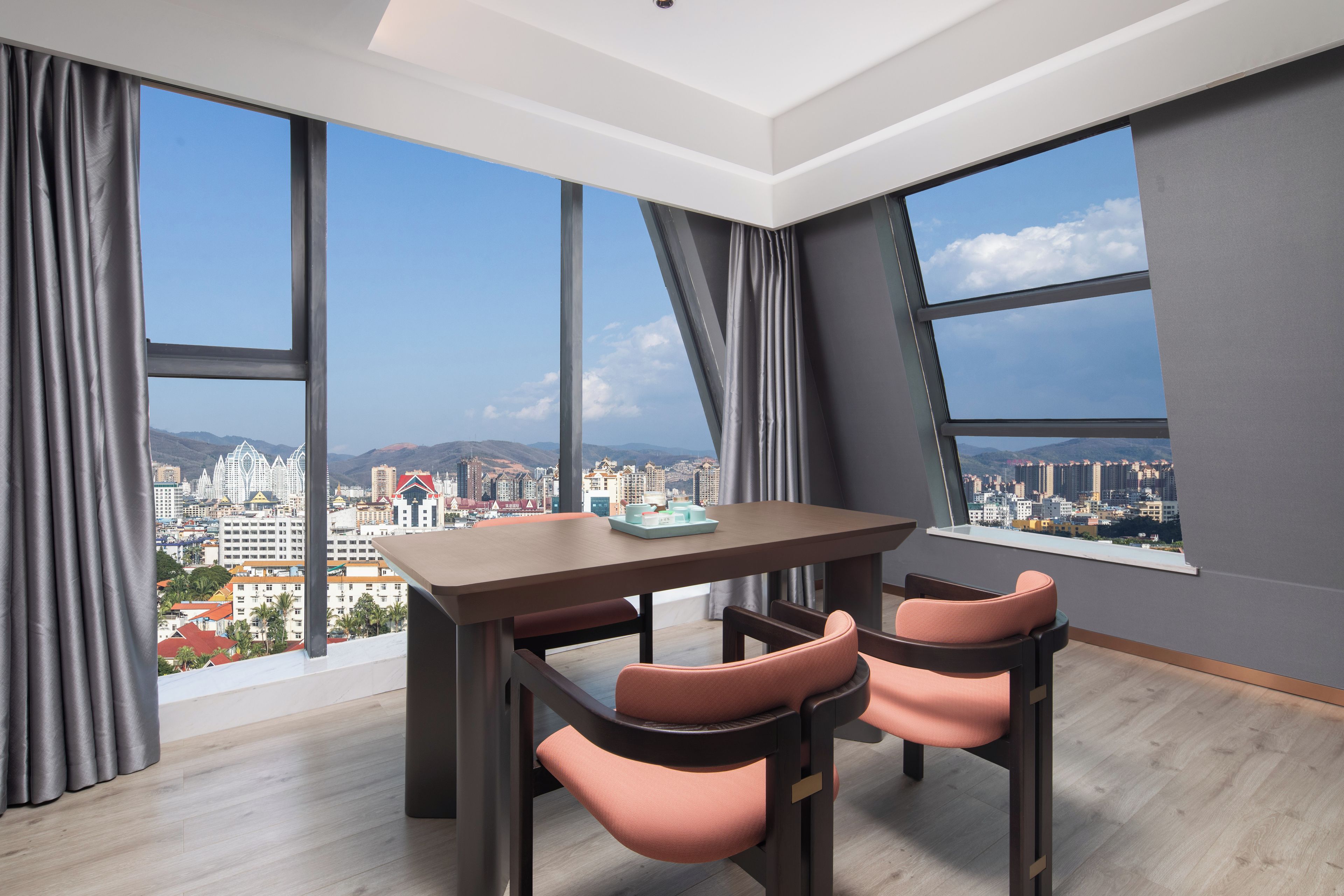 A modern room with a dining table and chairs, large windows with city views, and a wooden floor.