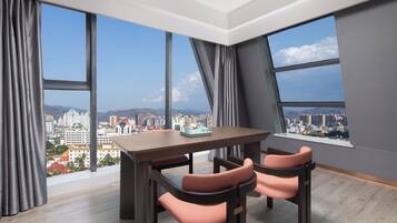 A modern room with a dining table and chairs, large windows with city views, and a wooden floor.