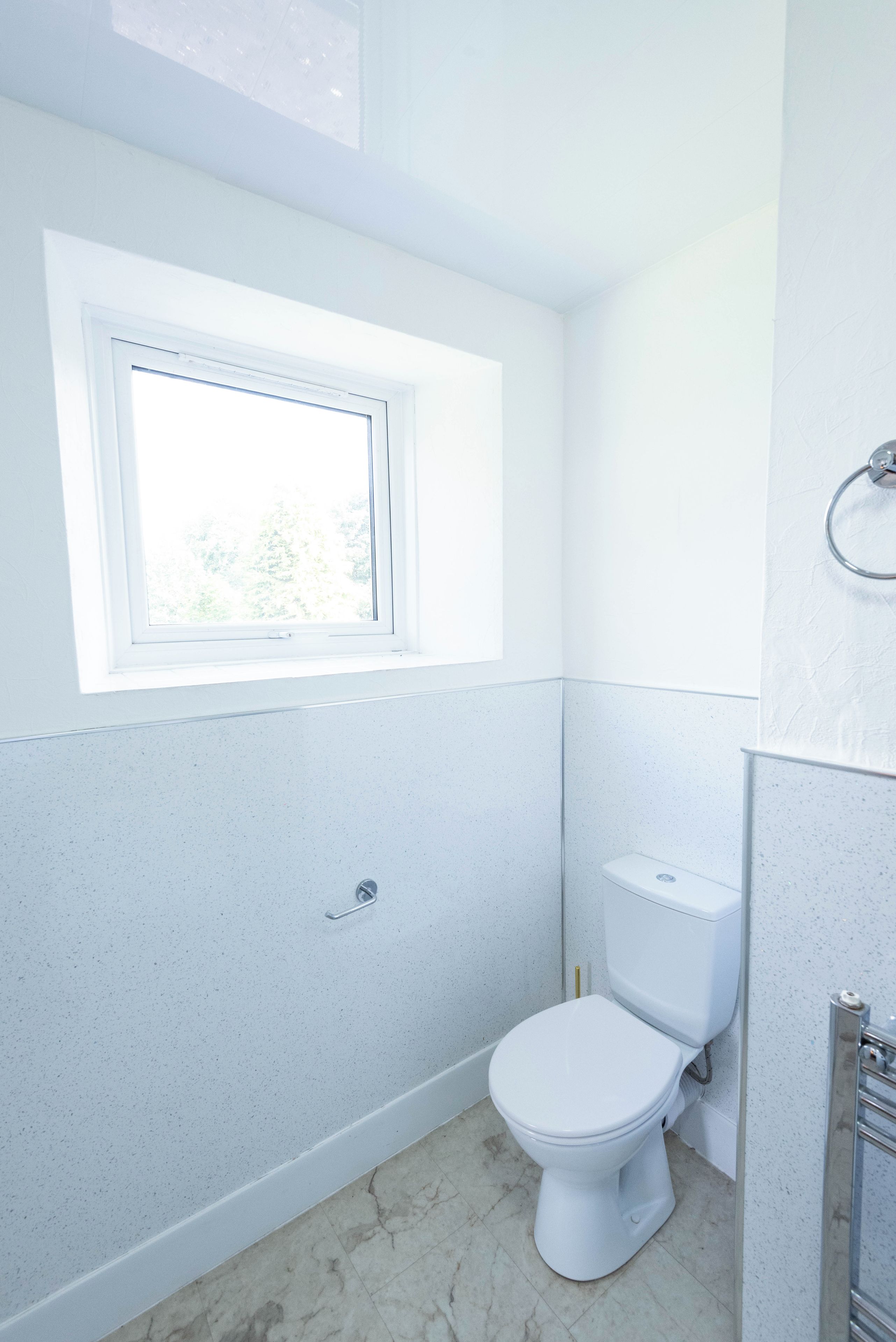 Une salle de bain avec des toilettes, une fenêtre et un porte-serviettes.