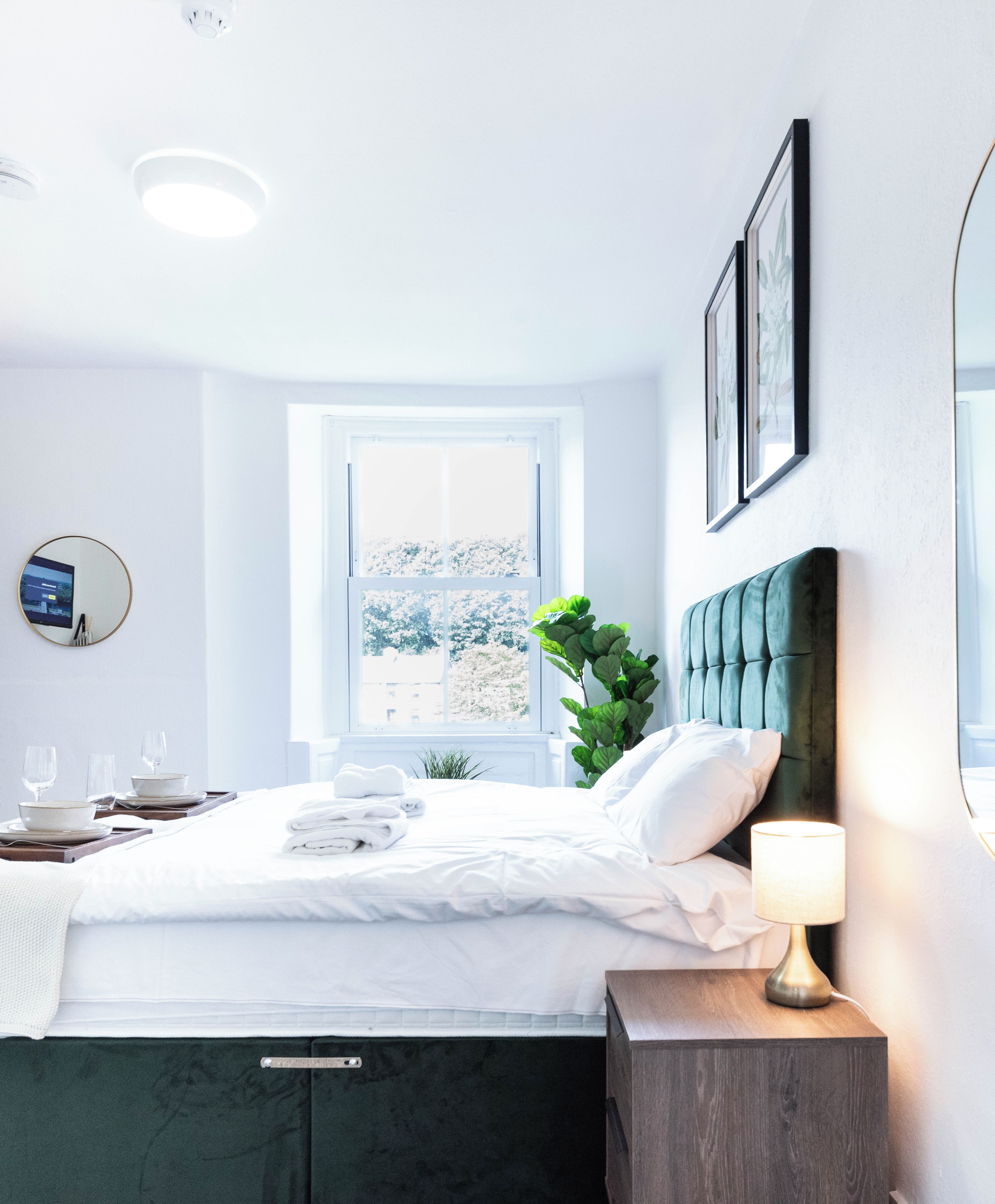 A hotel room with a bed, bedside table, lamp, and a large window.
